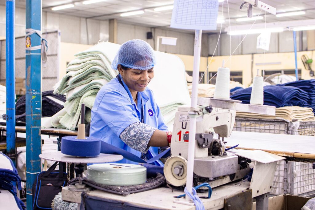 Female worker operates sewing machine in bright textile factory.