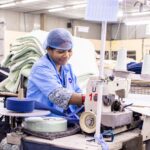 Female worker operates sewing machine in bright textile factory.