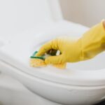 From above of crop anonymous person in rubber gloves using soapy sponge while cleaning toilet bowl