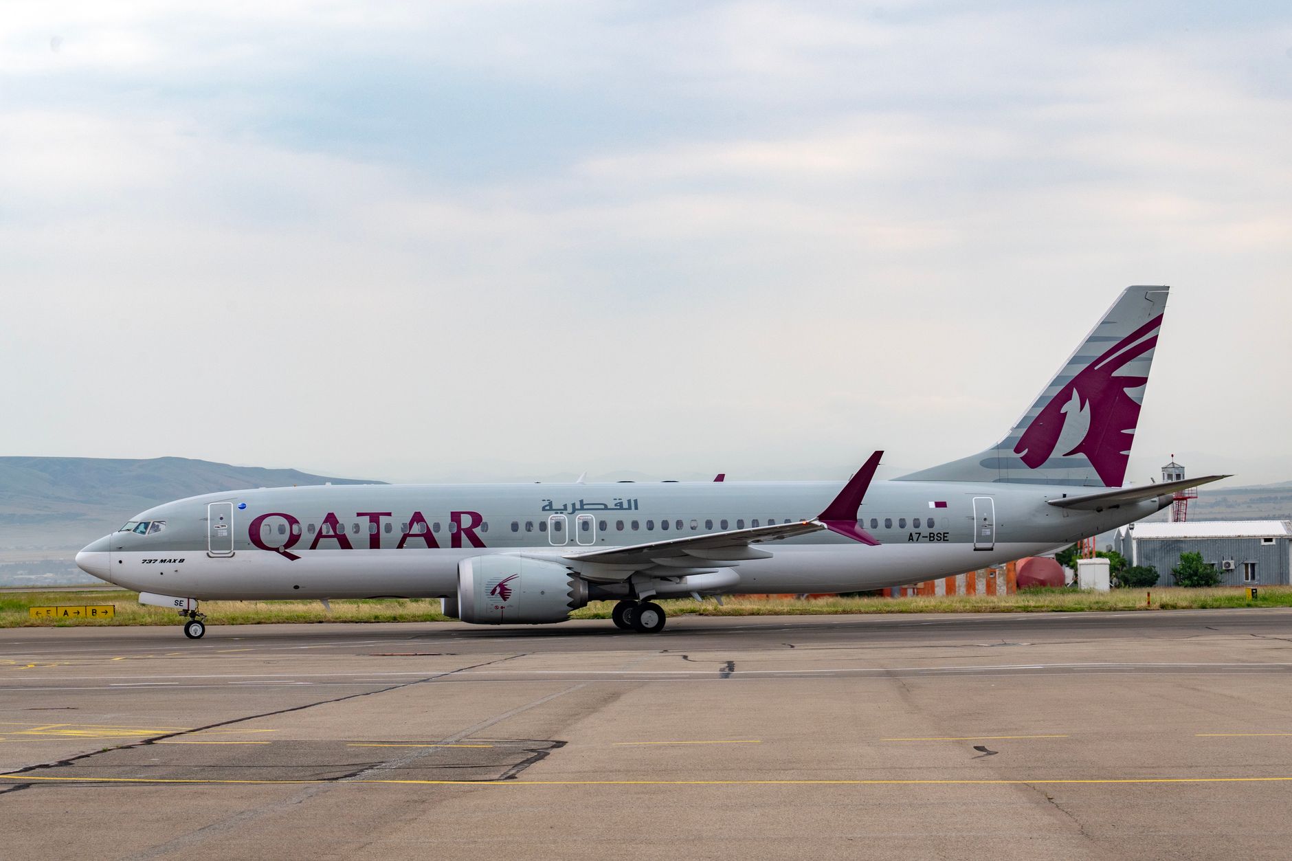 Qatar Airways aircraft captured on runway at Tbilisi airport. Clear sky and distant hills enhance the scene.