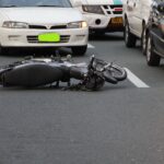 A motorcycle lies on a city road amidst traffic, indicating a recent accident.