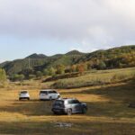 Explore the scenic valley landscape with off-road vehicles surrounded by lush hills and autumn foliage.