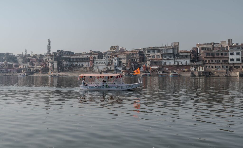 Boat cruising on the Yamuna River with Mathura cityscape in Uttar Pradesh, India.