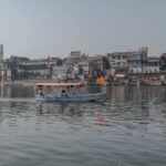 Boat cruising on the Yamuna River with Mathura cityscape in Uttar Pradesh, India.