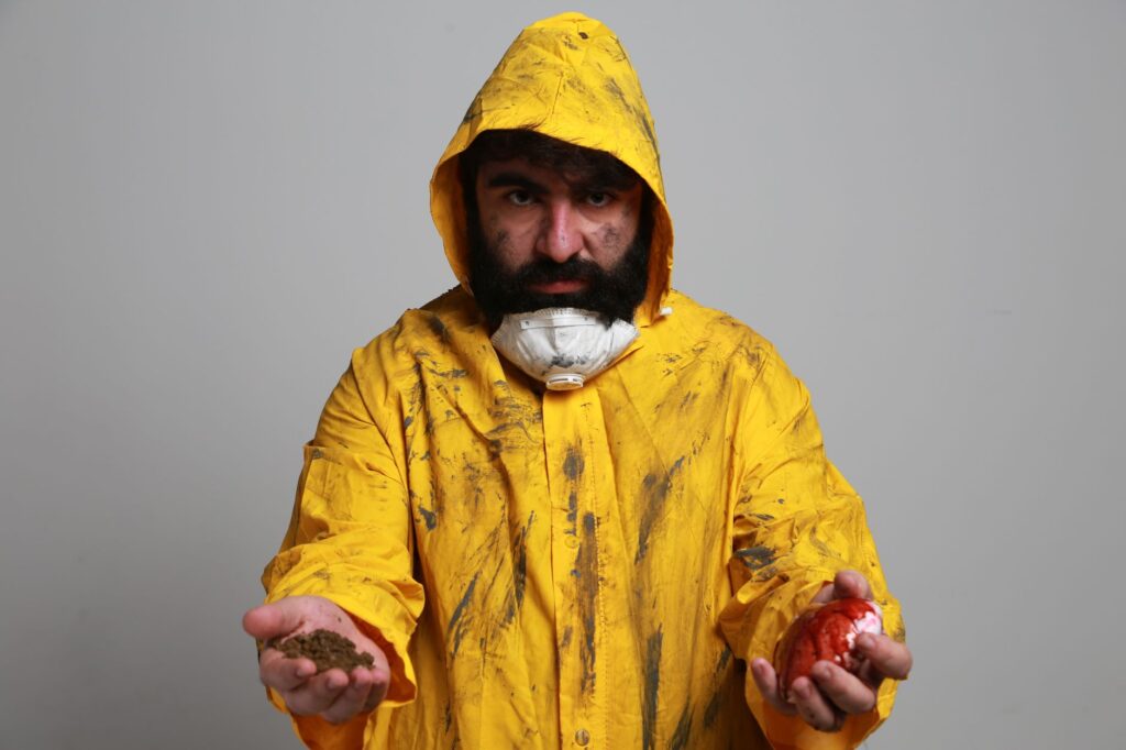 Portrait of a man in a yellow hazmat suit holding soil and a red apple, symbolizing contamination.
