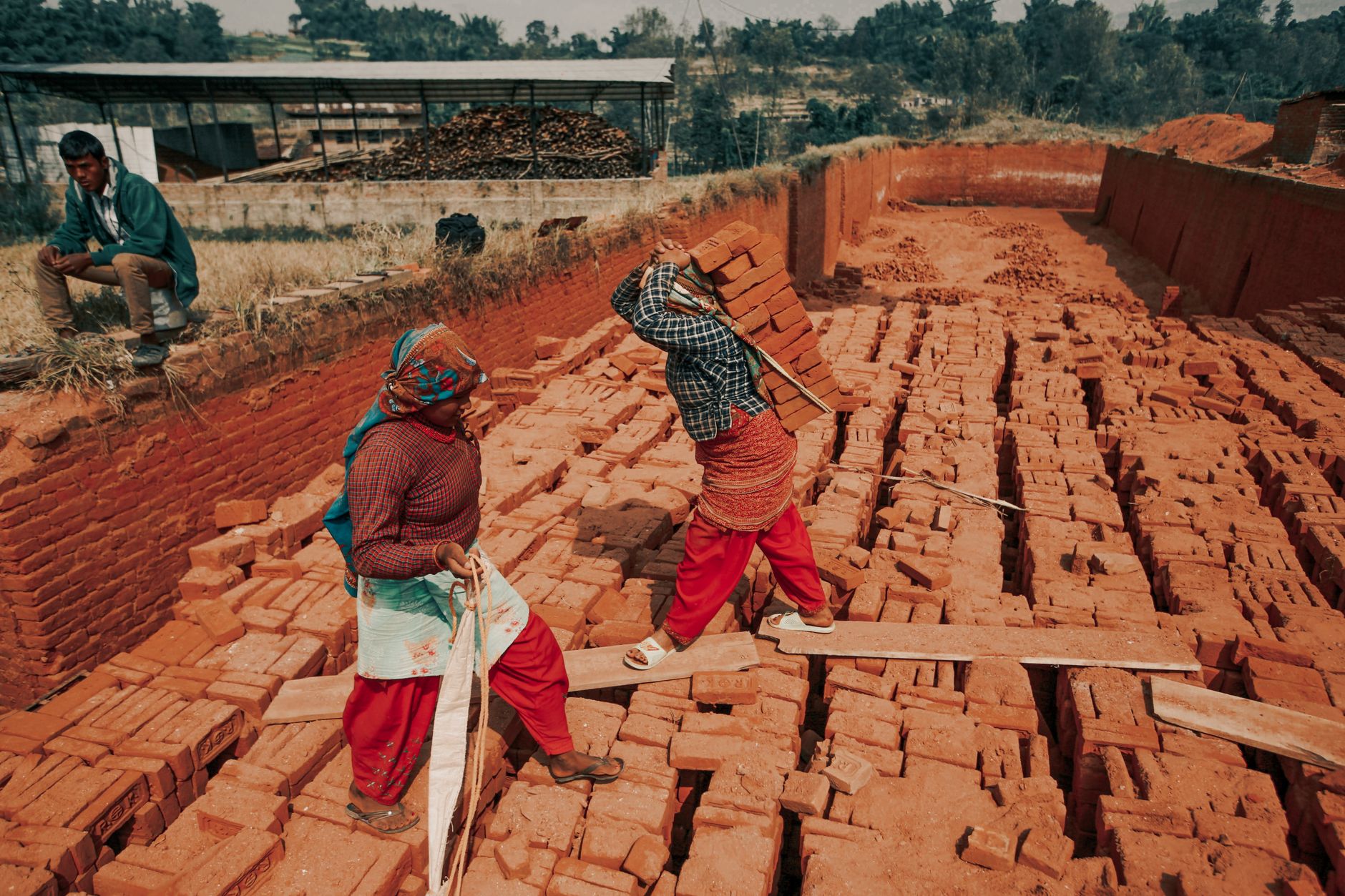 Two workers carrying bricks at an outdoor construction site, showcasing teamwork and labor.
