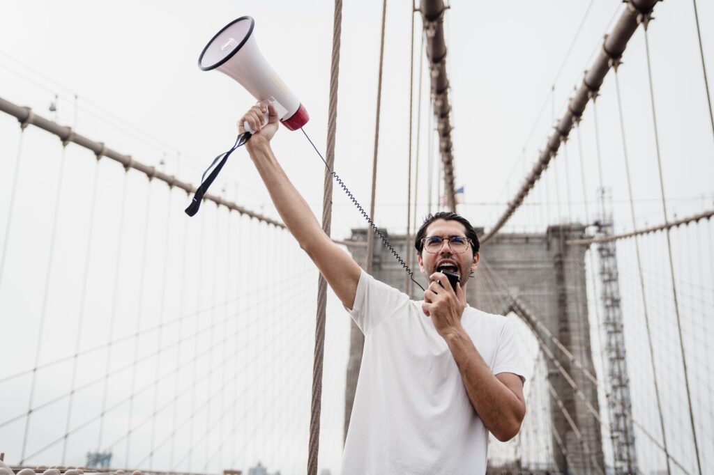 A protester holding a megaphone stands on a famous bridge, voicing support for a cause.