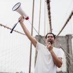 A protester holding a megaphone stands on a famous bridge, voicing support for a cause.