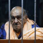Portrait of an elderly man behind bars wearing casual clothing, conveying a thoughtful mood.