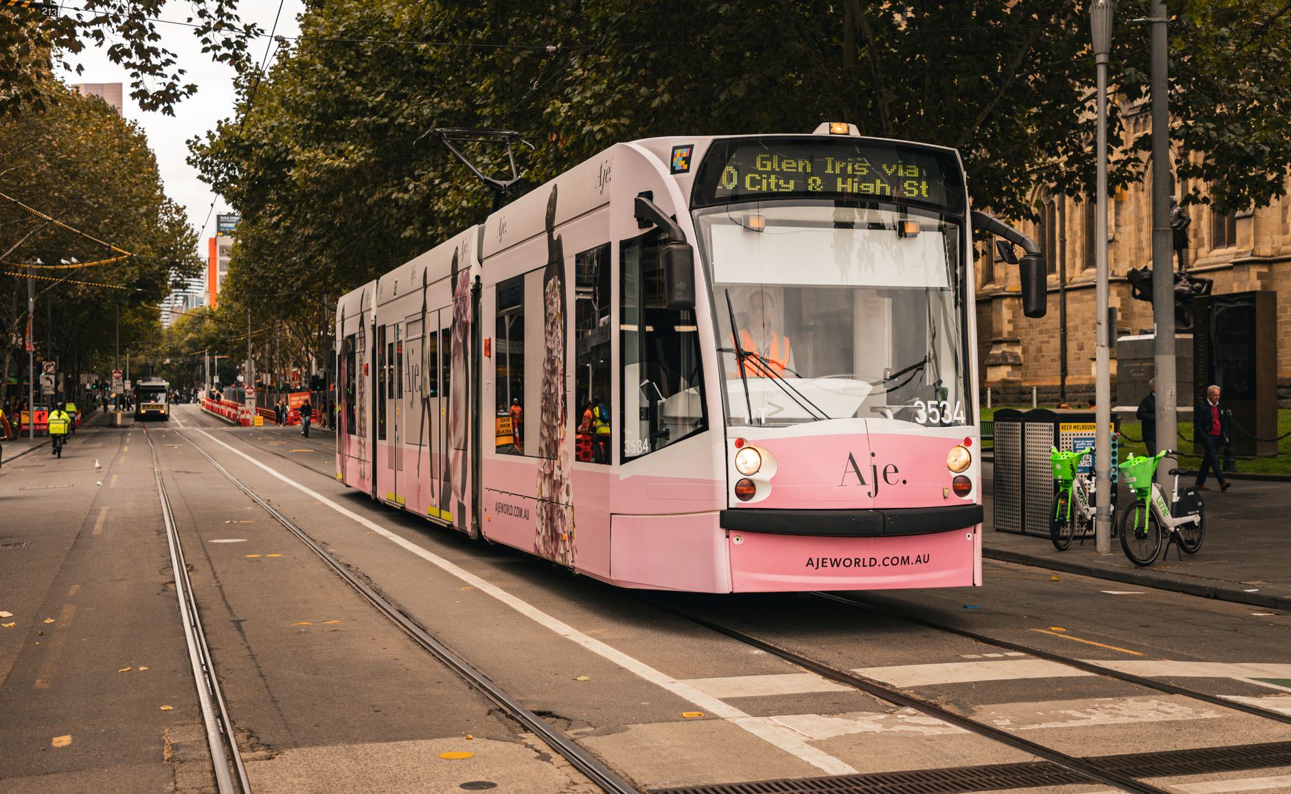 A vibrant pink tram travels down a tree-lined street in Melbourne, Australia.