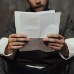 Close-up of a prisoner in uniform reading a letter in a cell setting, highlighting prison life.