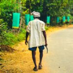 A man in a village road holding a tool, surrounded by nature in Chodavaram, India.