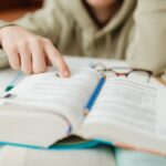 Focused student pointing at text in an open book, studying for exams indoors.