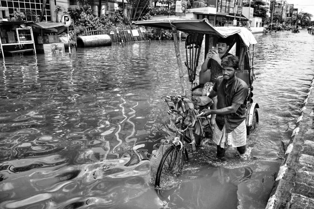 A rickshaw puller navigates through a flooded street in Kolkata, India, capturing resilience.