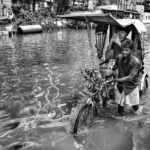 A rickshaw puller navigates through a flooded street in Kolkata, India, capturing resilience.