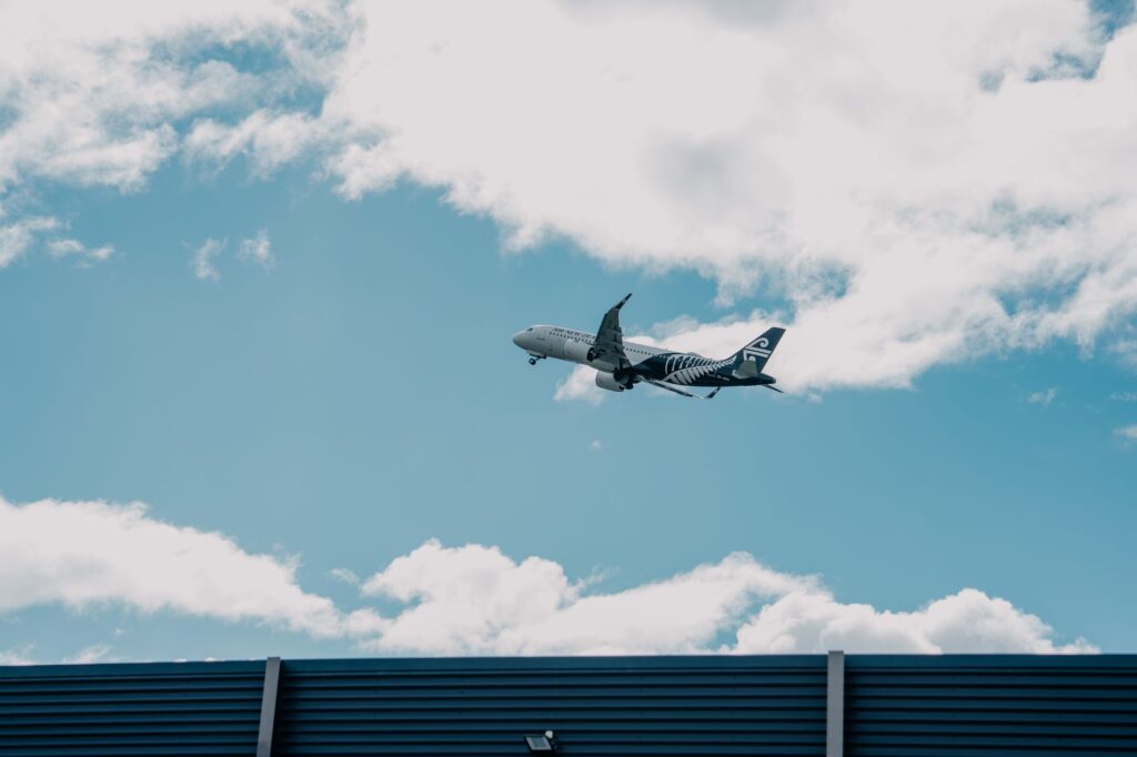 Airplane soaring above a building with cloudy skies in New Zealand.