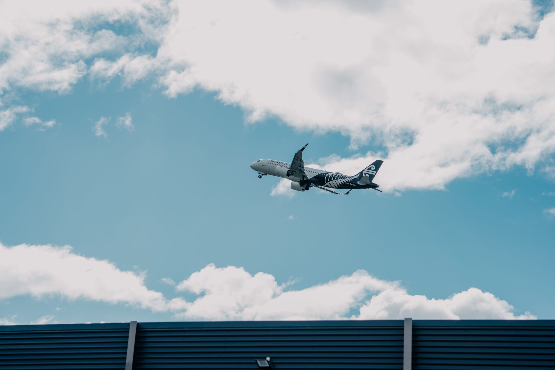 Airplane soaring above a building with cloudy skies in New Zealand.