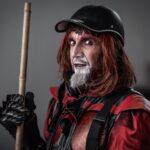 A dramatic street performer in a striking red and black costume with makeup.
