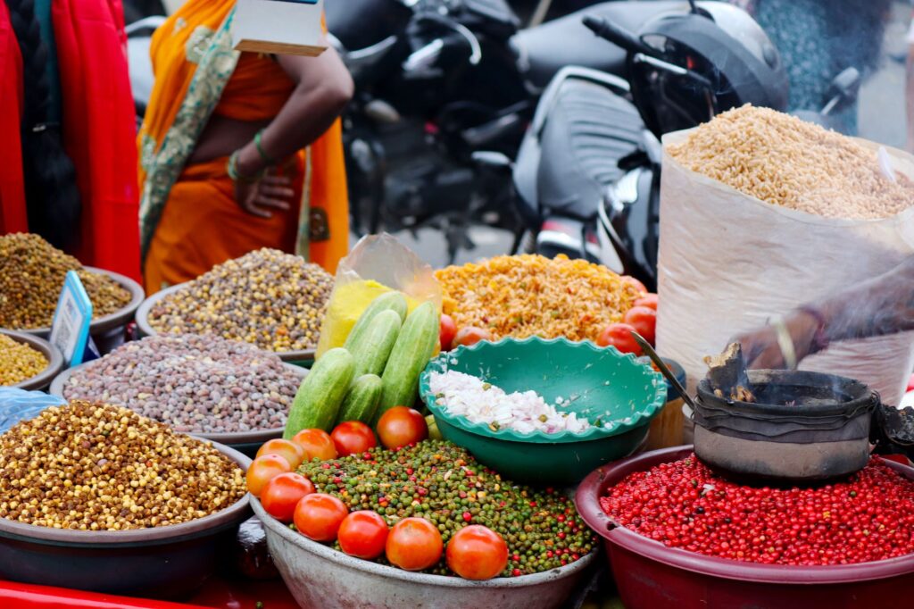 Colorful outdoor market stall featuring spices, tomatoes, cucumbers, and other vegetables.
