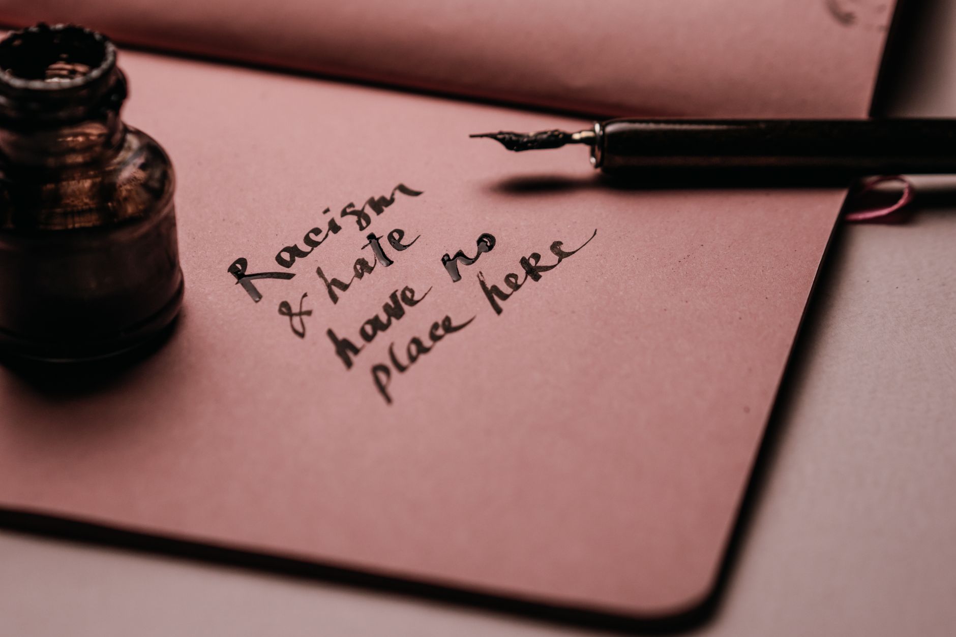 Ink pen and bottle on pink paper with motivational quote against racism and hate.