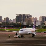 Airplane on a runway with a city skyline in the background, showcasing urban and air travel themes.