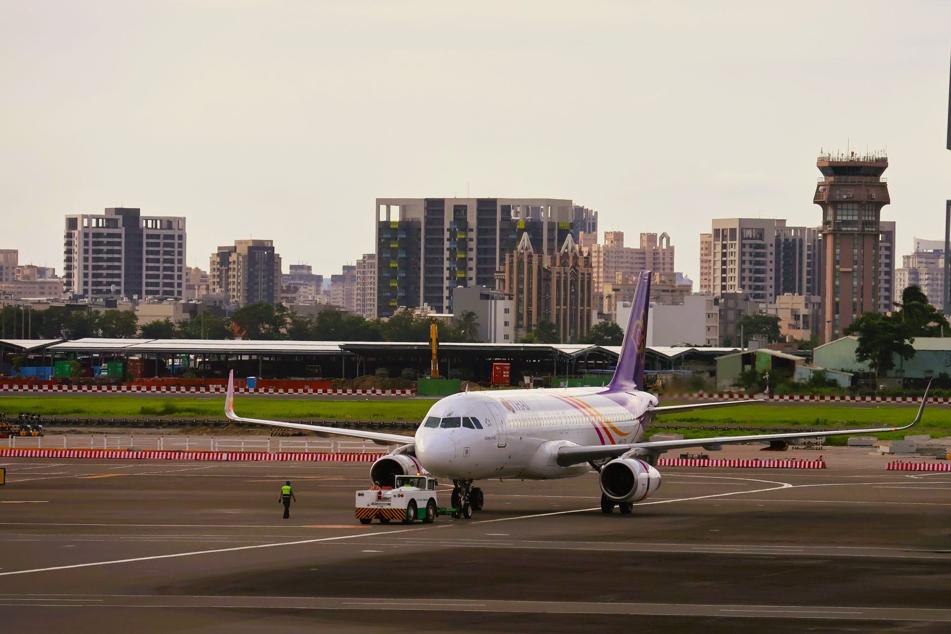 Airplane on a runway with a city skyline in the background, showcasing urban and air travel themes.