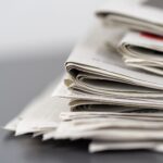 Close-up of stacked newspapers on a table, representing media and journalism.