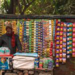 A street vendor stands at a vibrant stall selling various snacks on a busy street in India.