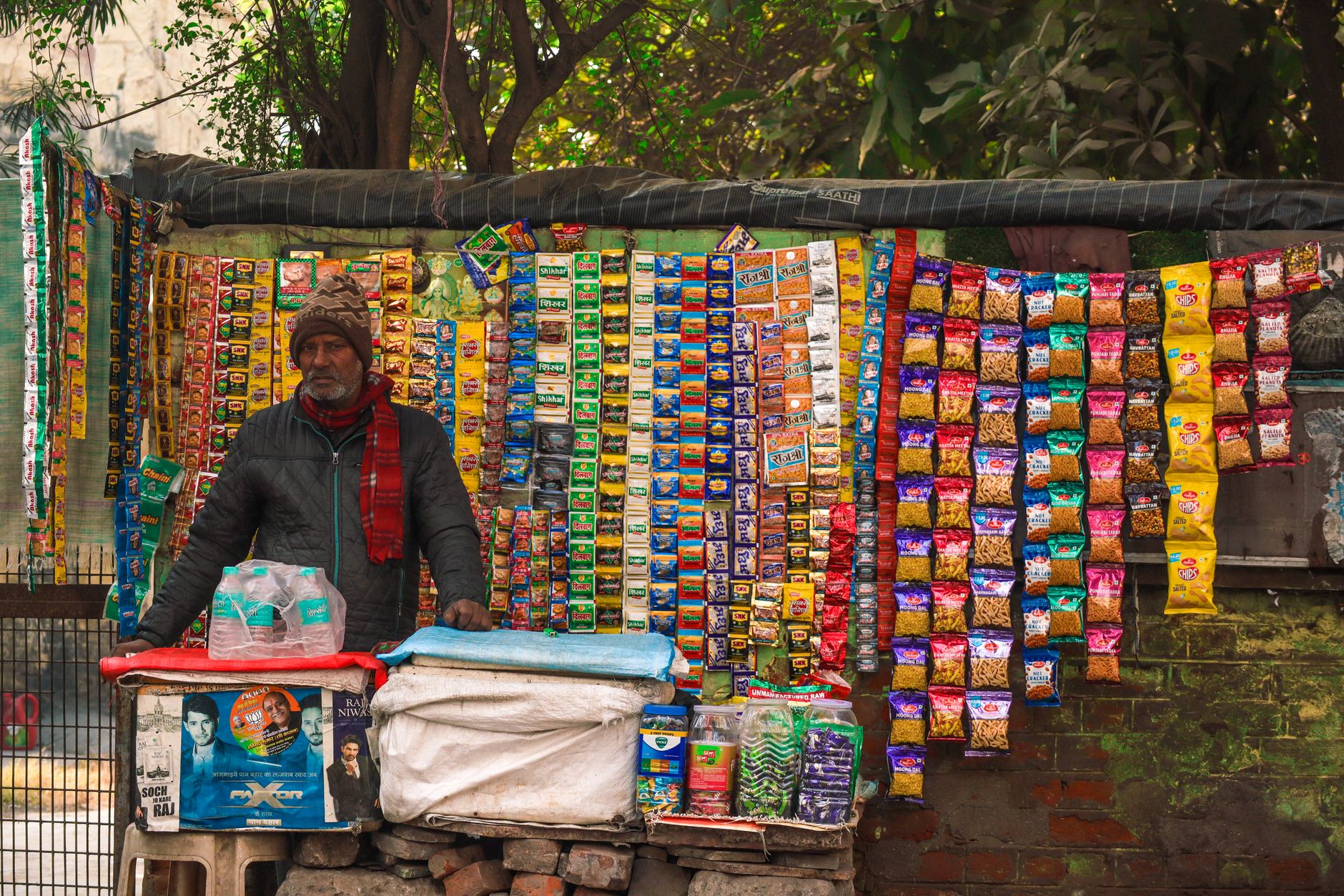 A street vendor stands at a vibrant stall selling various snacks on a busy street in India.