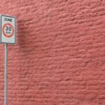 A 30 km/h speed limit sign against a textured pink brick wall in an urban setting.