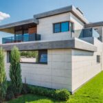 Contemporary two-story house with clean lines surrounded by green grass and blue sky.