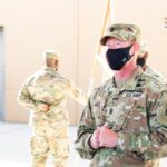 US Army soldiers in camouflage uniforms wearing masks outdoors during the day.