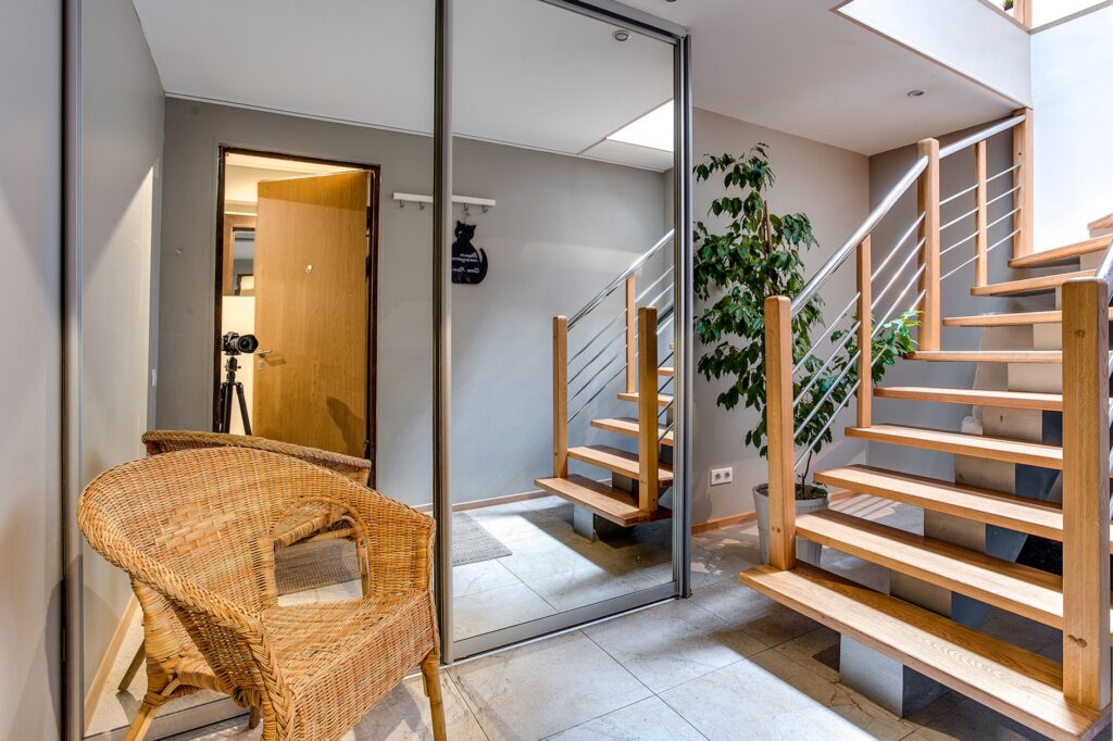 Contemporary home interior featuring a glass wardrobe, wooden staircase, potted plant, and rattan chair.
