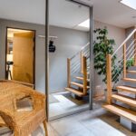 Contemporary home interior featuring a glass wardrobe, wooden staircase, potted plant, and rattan chair.