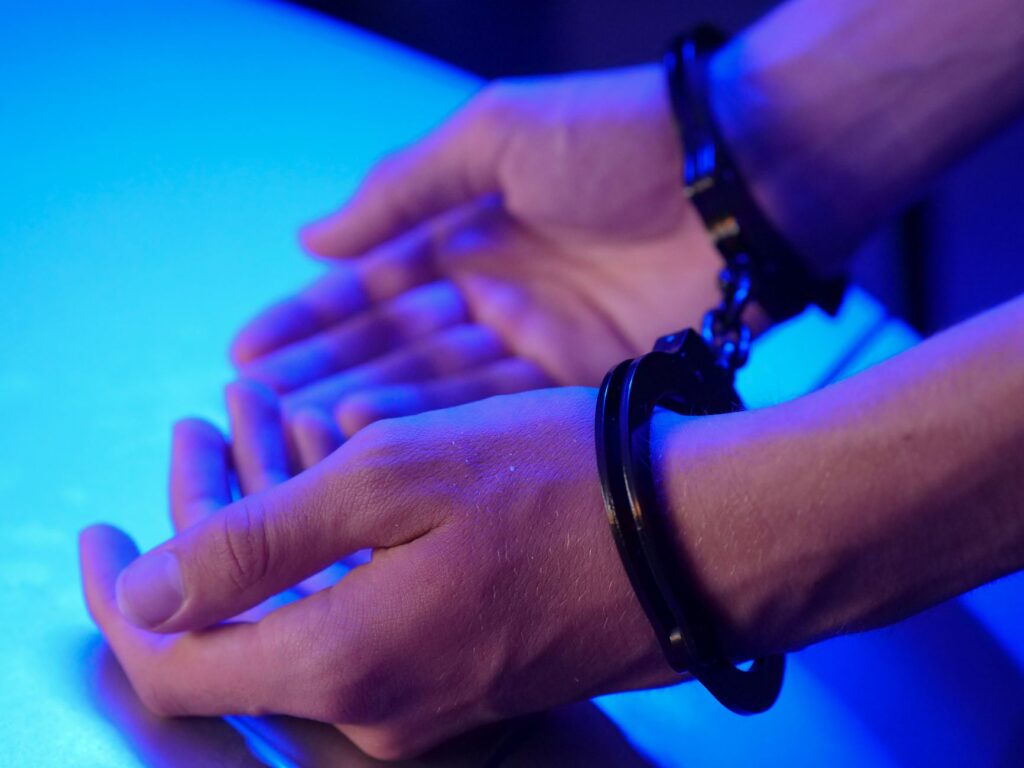 Close-up image of hands in handcuffs resting on a table under blue lighting depicting law enforcement.