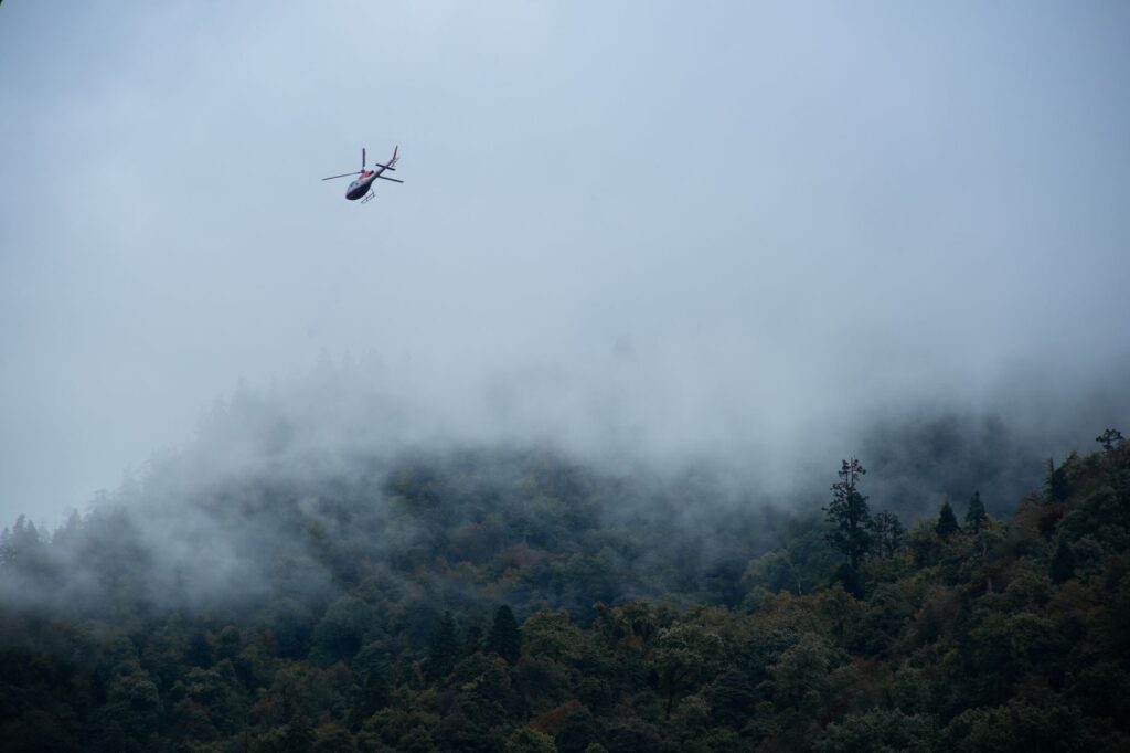 Aerial view of a helicopter flying over misty mountains in Ukhimath, India, capturing a serene and moody landscape.