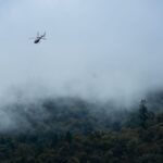 Aerial view of a helicopter flying over misty mountains in Ukhimath, India, capturing a serene and moody landscape.