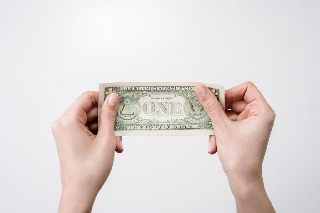 A close-up image of hands holding a one dollar bill, symbolizing finance and economy.