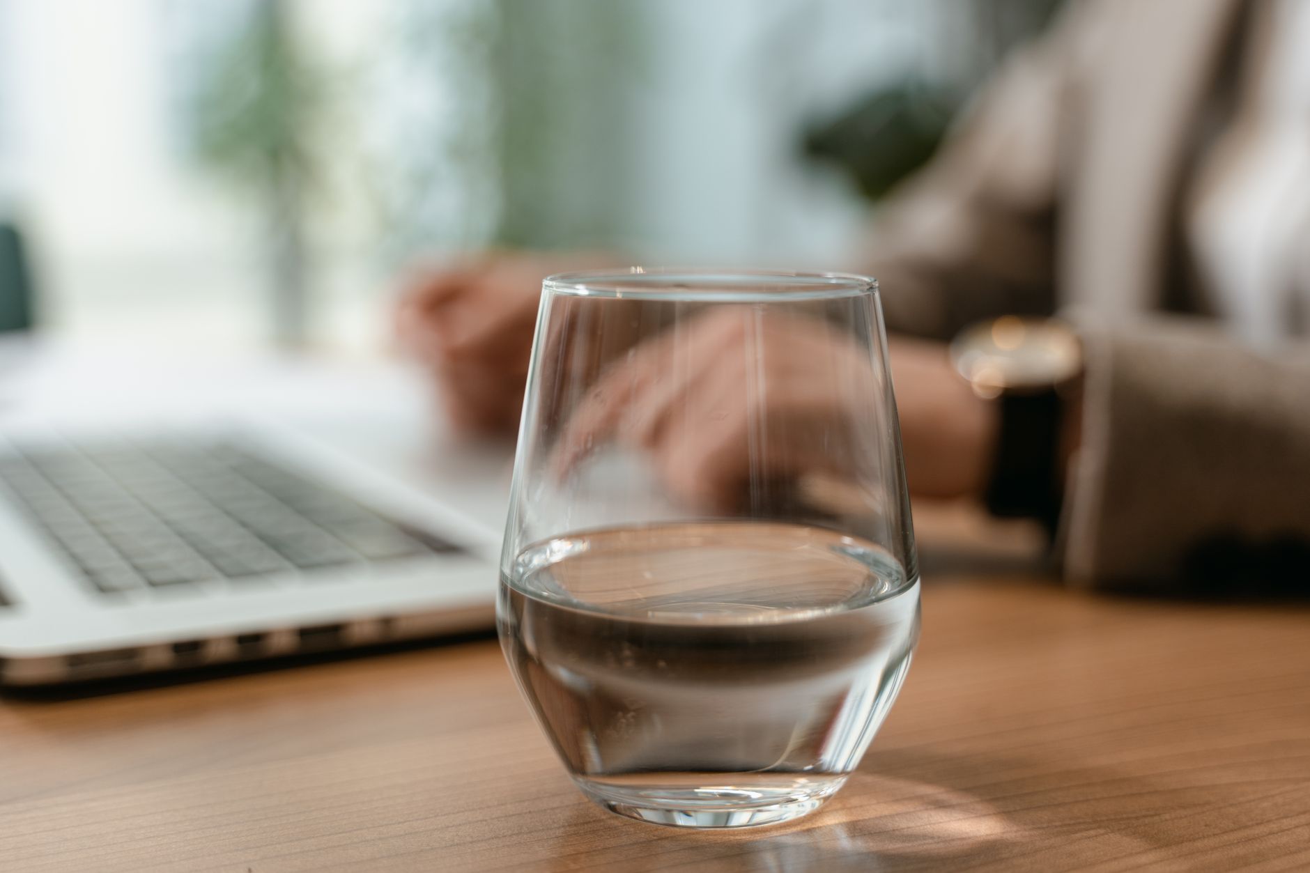 Close-up of a glass of water on a desk in an office setting with a laptop in the background.