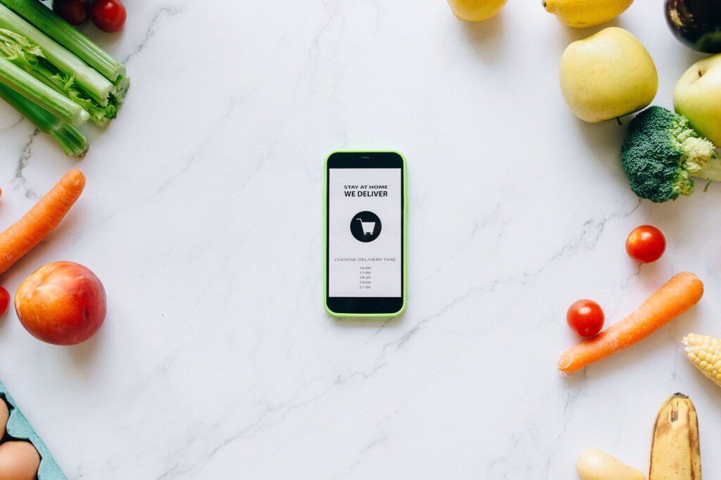 Mobile delivery app surrounded by fresh fruits and vegetables on a marble countertop.
